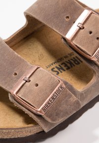 Bruna lädersandaler med två justerbara remmar och kopparfärgade spännen samt en texturerad korkfotbädd. Märkt "Birkenstock" inuti.