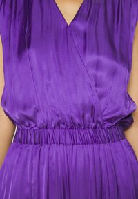 Robe en satin violet avec un décolleté en V, une taille élastique froncée et une jupe fluide. Texture lisse, tissu léger.