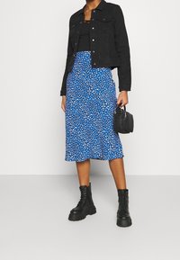 Czarna dżinsowa kurtka, czarny top na ramiączkach, niebieska spódnica midi w białe i niebieskie wzory, czarne masywne buty na sznurowadła, mała czarna torebka.