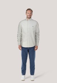 Witte overhemd met groene verticale strepen, lange mouwen, borstzak, gecombineerd met blauwe jeans en witte sneakers.