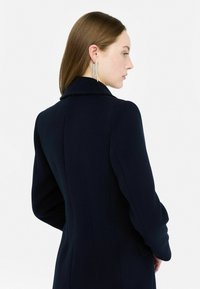 Marineblauw op maat gemaakt jasje met een gestructureerde kraag, lange mouwen en een getailleerd silhouet. Kenmerkt zich door een gladde stoftextuur en verticale naaddetails.