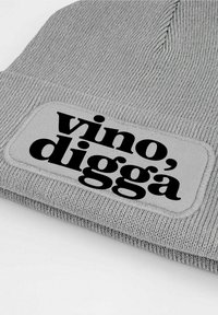 Gray knitted beanie with a textured finish, featuring a rectangular patch displaying the phrase "vino, digga" in bold black font.