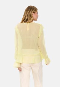 Sheer yellow blouse with ruffled sleeves and a high-low hem. Features a back keyhole opening and delicate texture throughout.