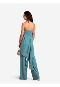 Teal jumpsuit met een strapless ontwerp, vloeiende overlay en gouden accentdetails aan de achterkant. Glad materiaal, wijde pijpen en een stijlvolle silhouet.