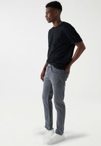 Camiseta negra de manga corta, jeans grises y zapatillas blancas. La camiseta tiene un pequeño logo; los jeans tienen bolsillos laterales y un ajuste slim.