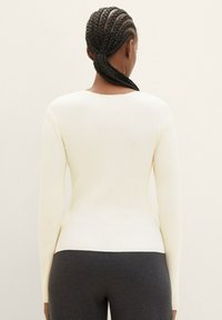 Långärmad krämfärgad ribbad topp med rundad halsringning, figurnära passform och sidoflikar, kombinerad med mörkgrå underdelar.