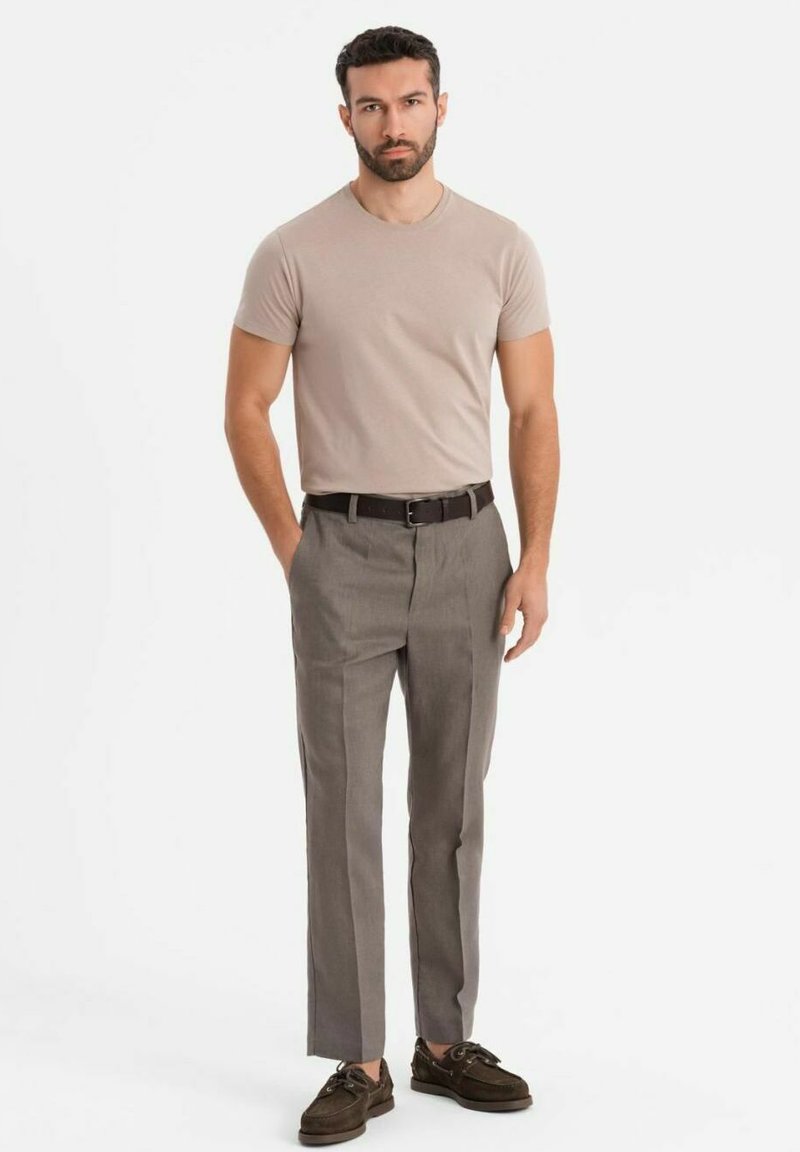 Béžové tričko, šedé kalhoty na míru a hnědé boty. Tento outfit se vyznačuje slim fit střihem, jemnou texturou a minimálním množstvím kovových detailů.