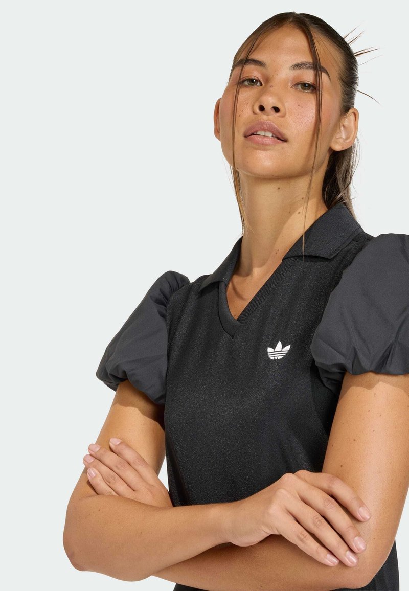 Blusa nera a maniche corte con scollo a V, caratterizzata da maniche a palloncino nere strutturate e logo bianco sul petto a sinistra. Tessuto dalla texture liscia.