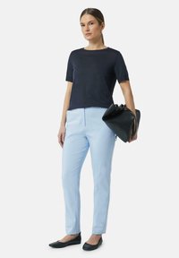 Marineblauwe shirt met korte mouwen, lichtblauwe tailor-pants, zwarte ballerina's en een zwarte handtas. Eenvoudige lijnen en effen kleuren domineren de outfit.