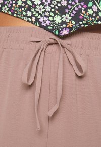 Pantalon mauve clair à texture douce, doté d'une ceinture élastique et d'un cordon de serrage. Le haut présente un motif floral sur un fond noir.