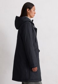 Czarna ocieplana parka z kapturem, posiadająca zamek z przodu, boczne kieszenie oraz prosty krój. Tkanina wydaje się gładka i matowa.