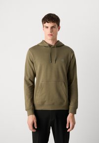 Olijfgroene hoodie gemaakt van zacht materiaal, met een voorzak, verstelbare capuchon en een subtiele logo patch op de borst.