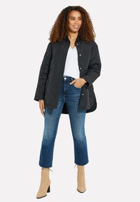 Chaqueta acolchada negra con botones a presión, camiseta blanca, jeans azules con dobladillo deshilachado y botas de tobillo marrón claro con tacón cuadrado.
