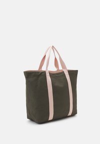 Zielona torba na ramię z płótna z jasnoróżowymi bawełnianymi paskami, kwadratowym kształtem, teksturowaną powierzchnią i kontrastowym wykończeniem wzdłuż górnej krawędzi.