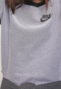 Nike grijs mesh T-shirt met een zwarte halslijn. Voorzien van een opvallend zwart logo op de borst. Lichtgewicht, ademende stof.
