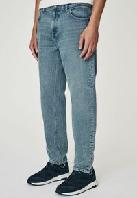 Blugi din denim bleu deschis cu croială dreaptă, design cu cinci buzunare și ușoară estompare. Asortați cu adidași negri cu talpă albă.
