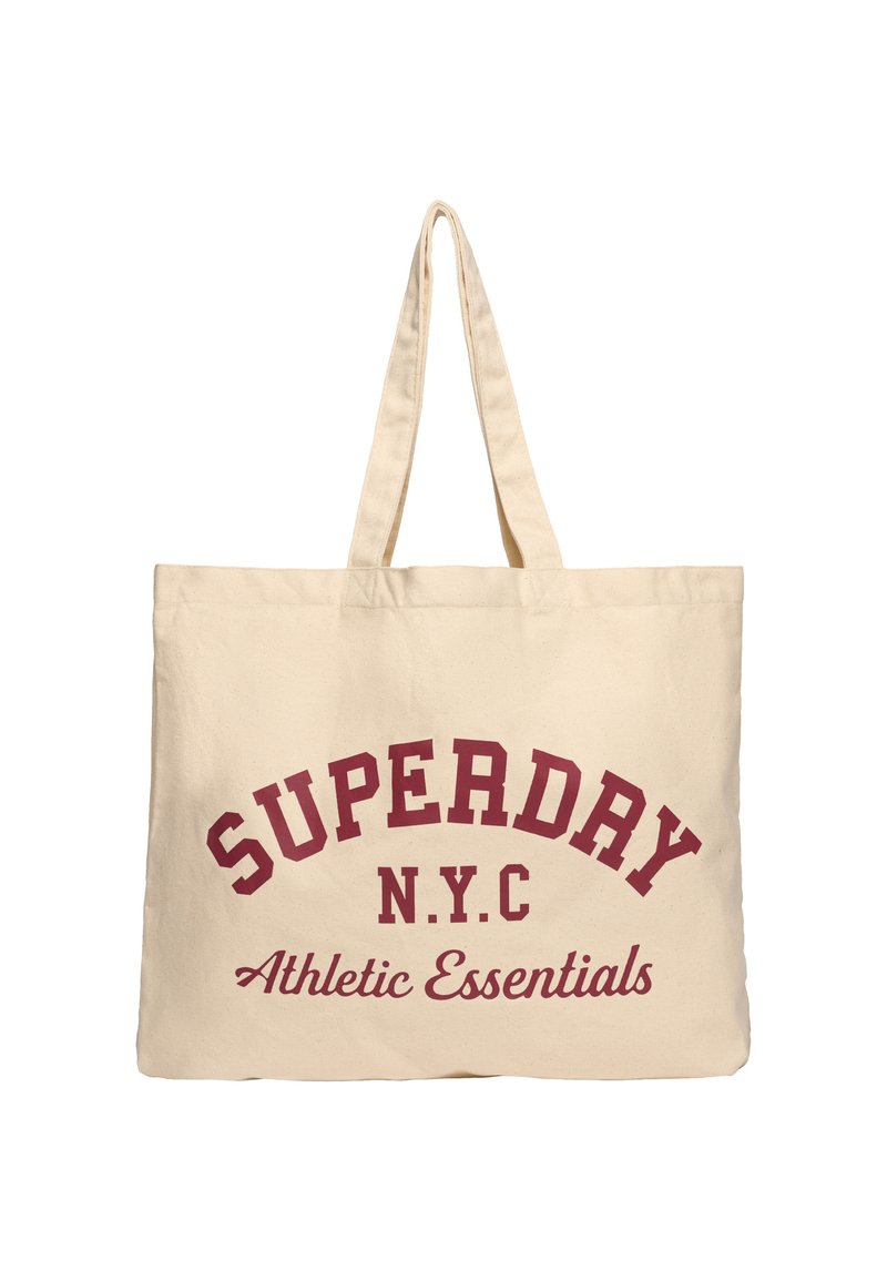 Sac en toile beige avec un texte incurvé rouge portant la mention "SUPERDAY N.Y.C Essentials Athlétiques." Il dispose de deux poignées robustes et d'une forme rectangulaire.