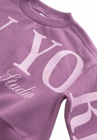 Felpa viola con bold lettering bianco. Presenta un collo e polsini a costine, una texture morbida e un design moderno e informale.