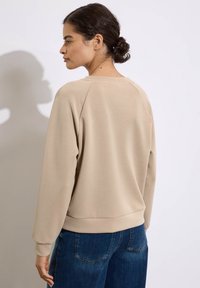 Felpa beige con maniche raglan, colletto a girocollo e polsini a coste, abbinata a jeans blu scuro dal taglio comodo con tasche posteriori.