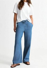 Světle modré kalhoty širokého střihu s elastickým pasem a šňůrkou. V kombinaci s volně střiženým bílým tričkem a hnědými sandály.