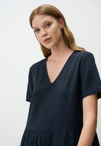 Ciemnoniebieska sukienka z dekoltem w kształcie litery V i krótkimi rękawami, wykonana z teksturowanej tkaniny, z marszczonym dołem, który dodaje objętości.