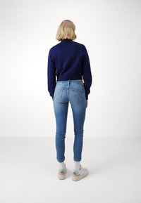 Marinblå kort cardigan med ribbade muddar, kombinerad med ljusblå högmidjade skinny jeans och vita chunky sneakers med pastellaccent.