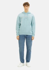Sudadera azul claro con un bolsillo tipo canguro y capucha con cordones, que presenta la impresión "Denim Tom Tailor" en el pecho. Combinada con unos vaqueros azules.