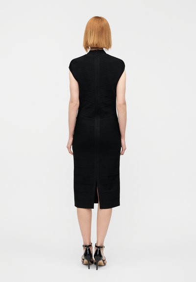 Μαύρο στενό φόρεμα με ψηλό λαιμό, κοντά μανίκια καπέλο και οριζόντια ριμπ υφή. Φερμουάρ στο πίσω μέρος και σκίσιμο στο τελείωμα. Φορεμένο με σανδάλια με τακούνι.