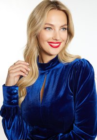 Samtkleid in königsblau mit hohem Kragen, einer Schlüsseleingabe und Knopfakzenten an den Ärmeln. Glatte Textur mit gepufften Schultern.