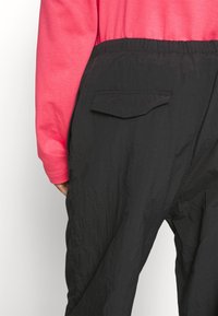 Pantalon noir à taille élastique avec une finition texturée, doté d'une poche arrière. Assorti à un haut à manches longues de couleur rose vif.