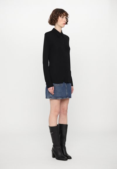 Svart langermet skjorte med knapper, kombinert med en blå denim miniskjørt og høyhælte støvler i svart lær som går opp til knærne. Enkelt stoff, tettsittende design.