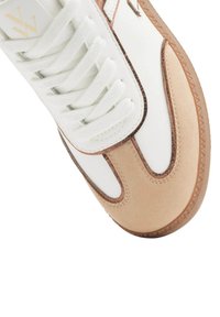 Baskets avec un dessus en cuir blanc et des accents en daim beige, bout arrondi et lacets plats blancs. Semelle en caoutchouc marron texturé.