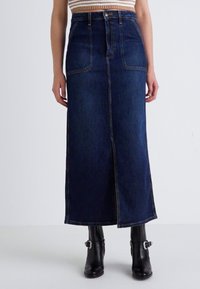 Dark blue denim maxi skirt with front slit, high waist, and two front pockets. Paired with black ankle boots featuring buckles.