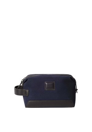 Navy blue canvas toiletry bag with a dark leather base and zipper. Features a side handle and a branded leather patch on the front.