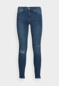 Jeans skinny azul escuro com uma textura suave, apresentando detalhes de rasgos nos joelhos e zíperes nos tornozelos para um ajuste ajustável.