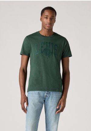Green cotton t-shirt featuring "LEVI'S" logo in a textured print, crew neck, and short sleeves, paired with light-wash denim jeans.