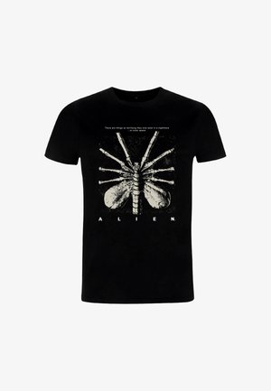 Camiseta negra de algodón con un diseño gráfico de huesos esqueléticos alienígenas y texto encima, diseño centrado. Mangas cortas, cuello redondo.