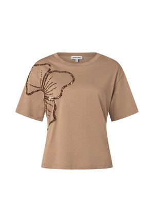 T-shirt beige à manches courtes avec un grand motif floral en sequins marron sur l’épaule gauche et la zone de la poitrine.