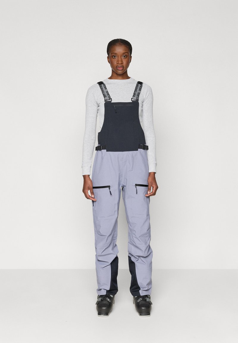 Smučarska kombinacija v mornarsko modri in svetlo sivi barvi, ki ima nastavljive naramnice, dve sprednji žepni zadrgi in prilega zasnovo, primerno za zimske športe.