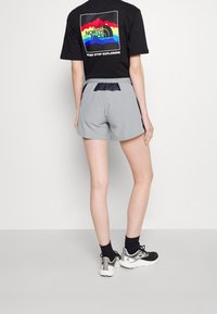 Grå shorts med elastiskt midjeband och svarta detaljer, kombinerat med en svart t-shirt som har en färgglad design på baksidan.