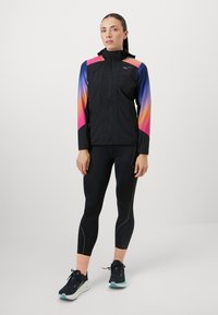 Könnyű fekete dzseki, gradiense rózsaszín és kék ujjak, cipzáros záródással és zsebekkel. Fekete leggingsszel és futócipővel viselve.