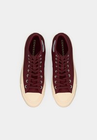 Baskets montantes en toile rouge avec un bout en caoutchouc crème et une semelle, œillets et lacets blancs, arborant le logo Converse sur la languette.