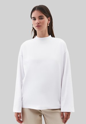 Wit shirt met lange mouwen, een hoge halslijn en een ontspannen pasvorm. Zachte textuur en een glad oppervlak, met doorgezakte schouders en een minimalistisch ontwerp.