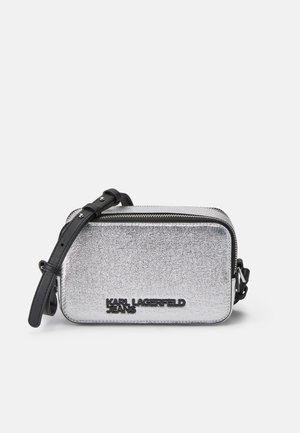 Silverfärgad metallisk crossbody-väska med dragkedjestängning, svart justerbar rem och präglad logotyp på framsidan. Rektangulär form, slät yta.