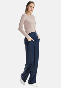 Light pink long-sleeve top with a cropped design paired with navy, wide-leg pants featuring side pockets. Smooth fabric texture, white sneakers.