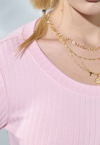 Pink ribbed top with a round neckline, paired with layered gold necklaces featuring various patterns and a small cross pendant.