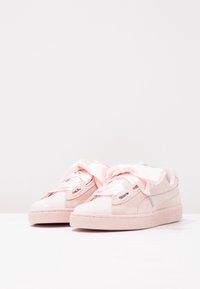 Světle růžové tenisky vyrobené z semišového a syntetického materiálu, s velkými saténovými šňůrkami, kulatou špičkou a texturovanou gumovou podrážkou.