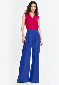 Dopasowany różowy top bez rękawów z dekoltem w kształcie litery V; niebieskie spodnie z wysokim stanem i szerokimi nogawkami, z zakładkami; gładka tekstura, żywe kolory.