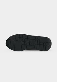 Semelle de chaussure en caoutchouc noir avec un motif de grille, vue de dessous sur un fond clair uni.