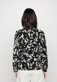 Svart långärmad blus med ett krämfärgat abstrakt mönster, rundad halsringning och smockade axlar för extra form och textur.